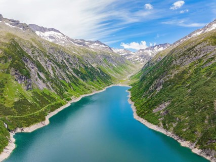 Mountain landscape with a blue lake in the centre, surrounded by lush greenery and snow-capped
