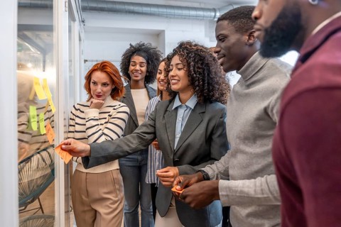 Hispanic woman sticking an adhesive note to a board during brainstorming in a coworking space
