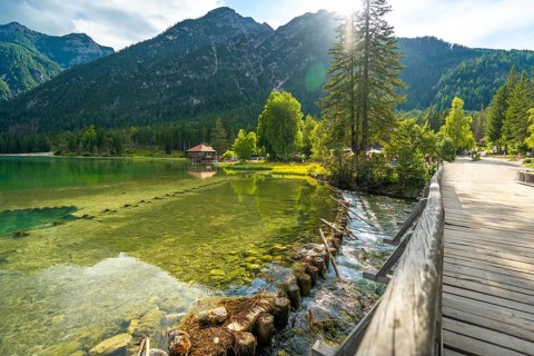 Sunlight illuminating the crystal clear waters of lake dobbiaco, with a wooden bridge and the