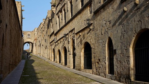 An ancient street lined with historic buildings with arcades in sunny weather and blue skies, moped