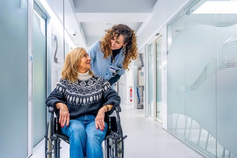 Young tender nurse talking to a mature injured woman in wheelchair in the hospital