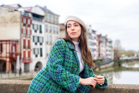 Cute woman in beret standing next to the river while visiting the city