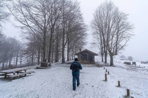 A young man walking next to the refuge of mount aizkorri in gipuzkoa. Snowy landscape by winter