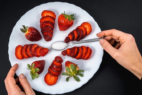 A woman's hand in a overhead view of natural strawberries on a white plate