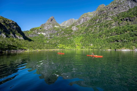 Two kayakers with red kayaks in the fjord Trollfjord, mountain peaks are reflected in the water,