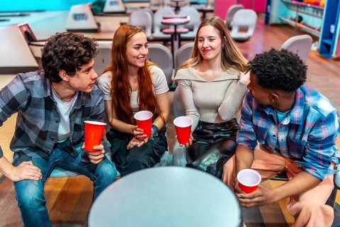 Four young friends enjoying a casual hangout at the bowling alley, holding red cups and engaging in