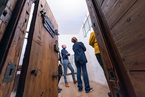 Several people standing in a room with large wooden doors and a historical appearance, Prison