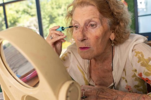 Senior woman applying mascara while gazing into a mirror, preparing for an outing. Embracing her