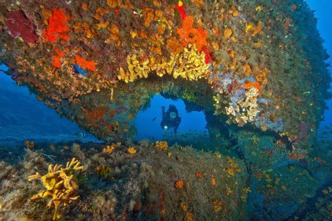 Diver looking through a hole Tunnel in underwater rocks at Capo d Orso on the north coast of
