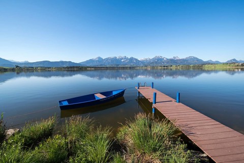 Blue sky over an alpine lake with a boat and a jetty, surrounded by mountains, Hopfen am See, near