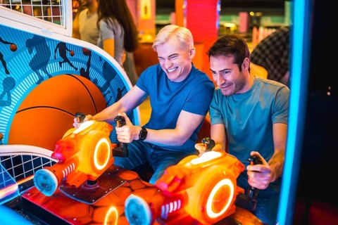Two male friends enjoying their free time playing arcade basketball simulator together, laughing