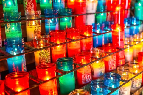 Colorful votive candles burning on a metal rack inside the montserrat monastery, creating a warm