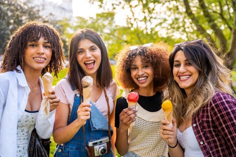 Four cheerful young women enjoying ice cream cones together in a park, celebrating summer and