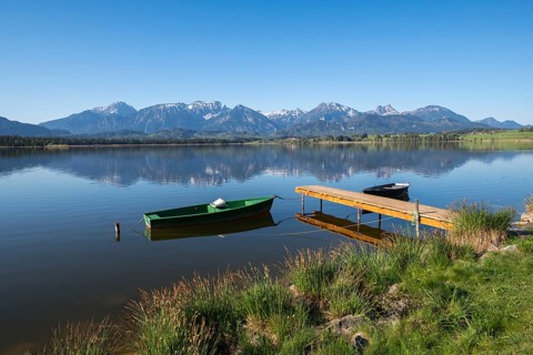 Jetty with green and black boats on a quiet lake in front of a mountain panorama, Hopfen am See,
