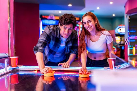 Multiethnic friends having fun together playing air hockey in a colorful amusement arcade