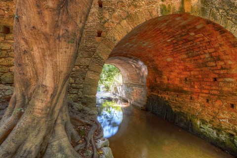 Stone tunnel with large tree next to it, quiet watercourse, Rodini Park, municipal park, Rhodes