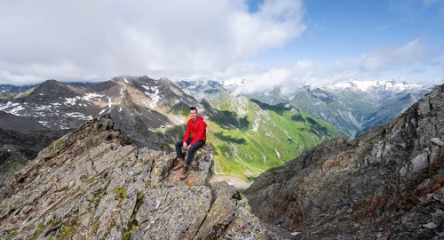 Mountaineer sitting on a rock, on a steep rocky ridge, on the summit of the Lasörling, view of the