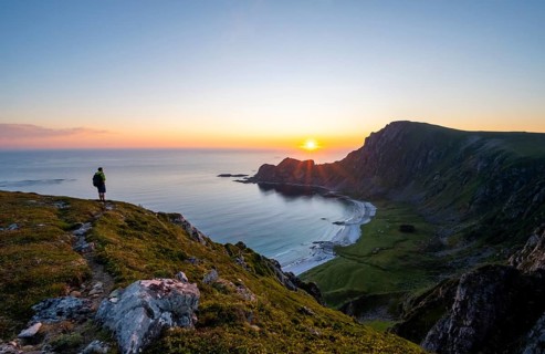 Mountaineer in front of view of coastal landscape at sunset, cliffs and summit of Måtind or