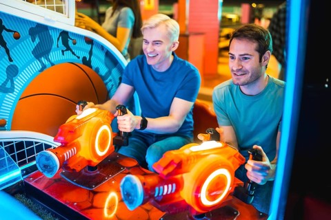 Two young men enjoying a friendly competition on an arcade game machine, illuminated by colorful
