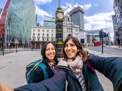 Two happy tourists taking a selfie in london near a historical clock tower, with modern buildings