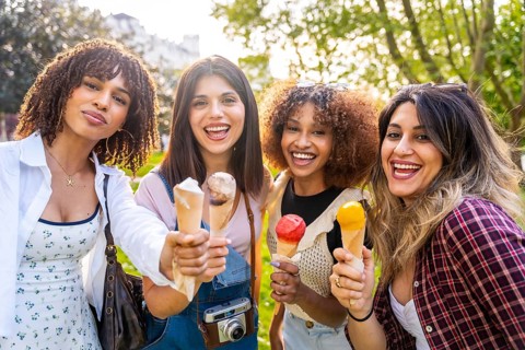 Four cheerful young women enjoying ice cream cones together in a park, celebrating friendship and