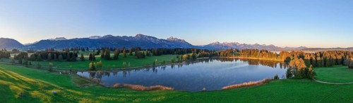 Panoramic view of a lake surrounded by forests and mountains at sunset, Hergratsrieder See, Alps,