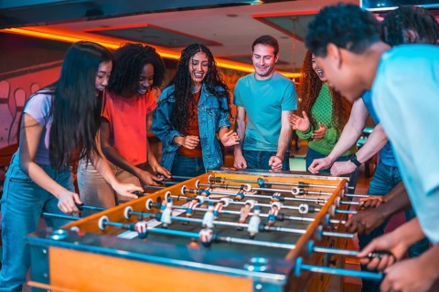 Cheerful multi ethnic friends enjoying a foosball table game in a vibrant entertainment center