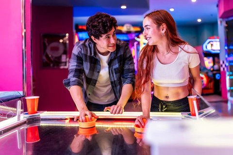 Happy multiethnic friends enjoying a weekend together, playing air hockey in a colorful and dynamic