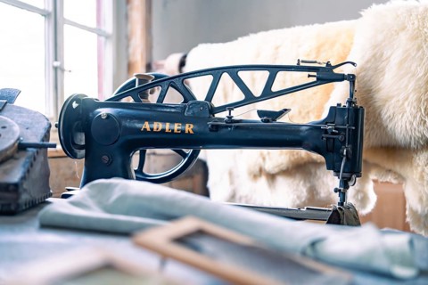 An antique Adler sewing machine in a studio with sewing accessories and leather material, Calw
