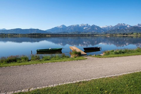 Calm lake with green and black boats, jetty and alpine landscape in the background, Hopfen am See,