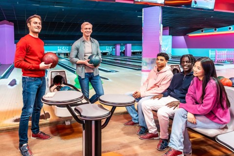Multi ethnic group of friends enjoying a lively bowling game at the alley, sharing laughter and