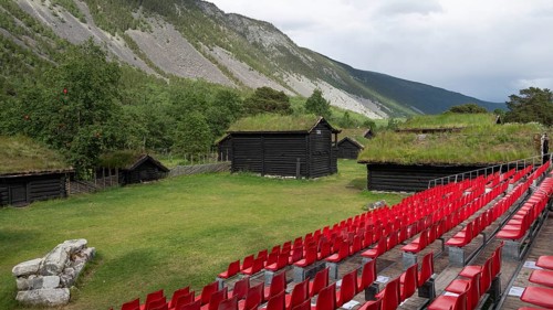 Traditional wooden houses with grass sod roofs, rows of seats with red plastic chairs, ready for an