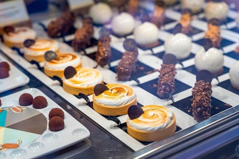 Mouth watering pastries and small cakes are neatly arranged on display in a bakery window, tempting