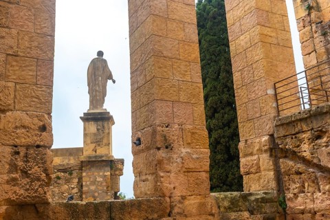 Ancient roman ruins with a statue and cypress tree in tarragona, spain, showcasing historical