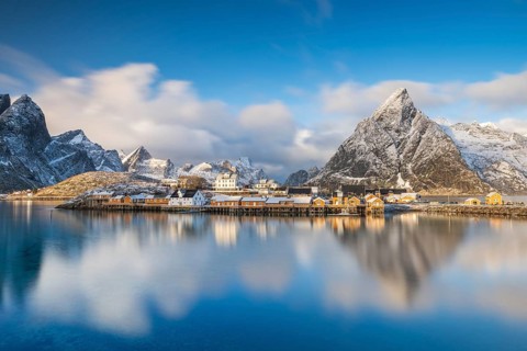 Traditional yellow rorbuer huts on the island of Sakrisøy, snow-capped mountains in the background,