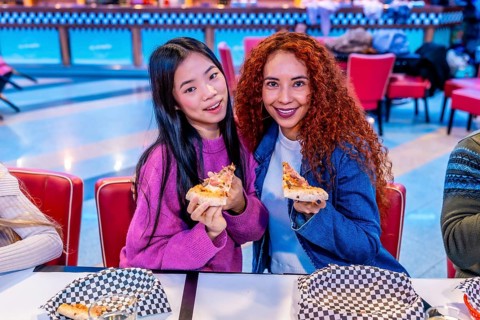 Two young women enjoying pizza slices at a bowling alley restaurant, celebrating friendship and