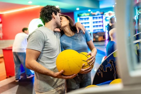 Romantic couple kissing while enjoying basketball and bowling in a vibrant entertainment center,