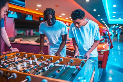Two young men concentrating on playing foosball in a brightly lit entertainment center, enjoying a