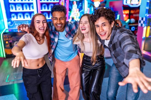 Four young multiethnic friends are enjoying their weekend together at an arcade, playing games and