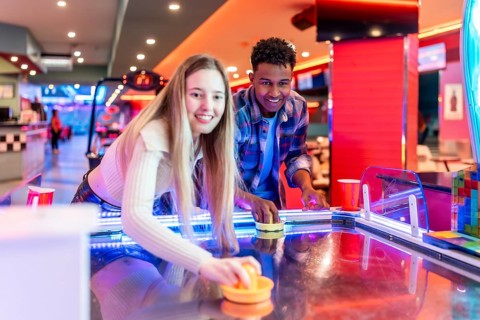 Two young friends enjoying a game of air hockey in a vibrant entertainment center, showcasing
