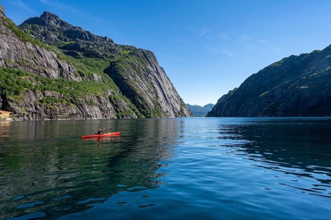 Kayaker with red kayak in the fjord Trollfjord, mountain peaks reflected in the water, fjord