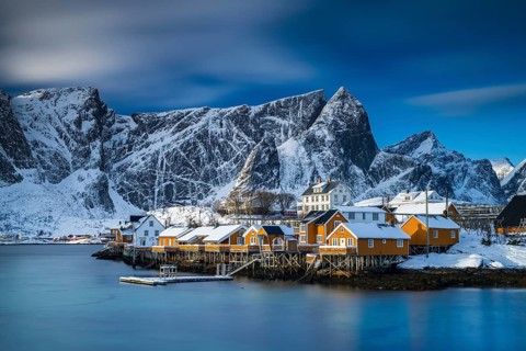 Traditional yellow rorbuer huts on the island of Sakrisøy, snow-capped mountains in the background,