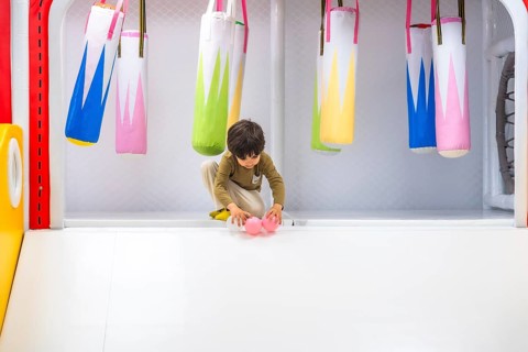 Preschooler playing with pink plastic balls in a colorful soft play area with small punching bags