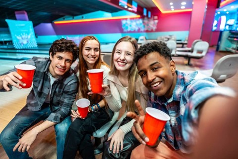 Group of cheerful young multiethnic friends taking a selfie while enjoying drinks and bowling at