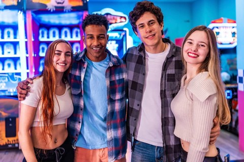 Four young multiethnic friends are smiling and having fun at an arcade, enjoying various games and