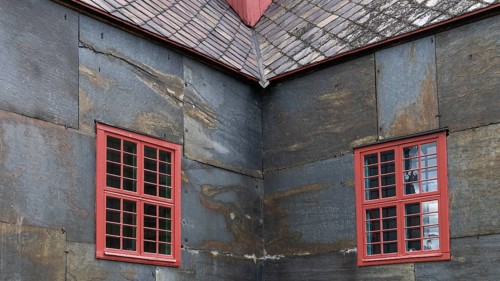 Detailed view of a corner of a building with red window frames on slate-clad walls, Dovre church,