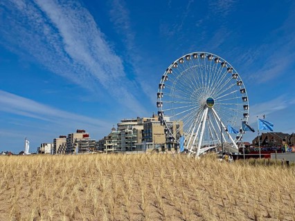 Ferris wheel next to modern buildings on the beach under a clear blue sky with clouds, Noordwijk,