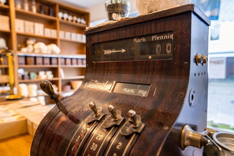 Antique cash register in a shop with ceramics and wooden shelves in the background, Calw Tannery