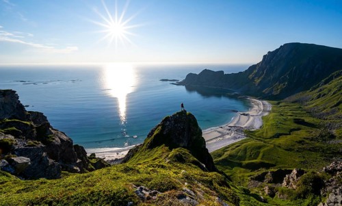 Climber on a rock, view of picturesque coastal landscape with sun star, steep coast with peak