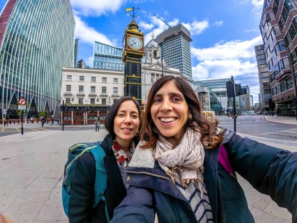Two happy tourists taking a selfie with a fisheye lens in front of a historic clock tower in